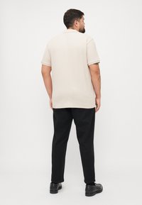 Beige short-sleeve polo shirt with a textured weave, paired with black trousers and black shoes; shown from the back against a white background.