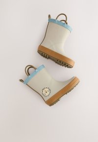 Stivali da pioggia in gomma beige per bambini con rifinitura blu, suole marroni, manici per tirare e grafica di un volto di leone sul lato.