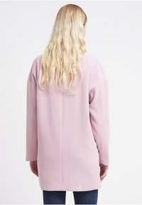 Long-sleeved, oversized pink top with a textured finish and a straight cut, featuring a back seam and minimalistic design details.