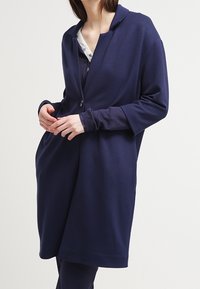 Marinblå oversized jacka i mjukt material, med slagkrage, långa ärmar och två framfickor. Knäppning framtill.