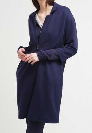 Námořnická modrá oversized bunda vyrobená z měkké tkaniny, s klopovým límcem, dlouhými rukávy a dvěma předními kapsami. Zapínání na knoflíky v přední části.