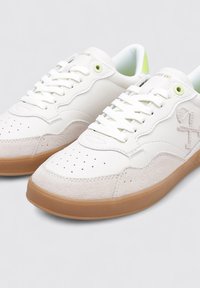 Baskets en cuir blanc avec des accents en suede gris clair, bout rond, détails perforés, lacets blancs et semelle en caoutchouc marron. Détail œillet vert.