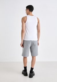 Bílá bezrukávová tílko spárované se šedými kraťasy po kolena vyrobenými z jemného materiálu. Černé ponožky a masivní boty doplňují celkový outfit.