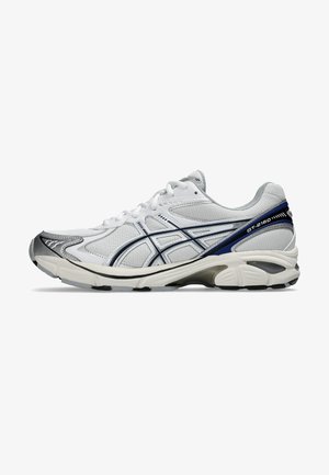 Weißer Sportschuh mit einem Mesh-Obermaterial, grauen Akzenten und blauen Details. Besitzt eine gepolsterte Sohle und eine verstärkte Zehenpartie für Stabilität.
