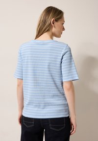 Ljusblå randig kortärmad topp med rund halsringning och en texturerad tyg. Ränderna är horisontella och har ljusare nyanser.