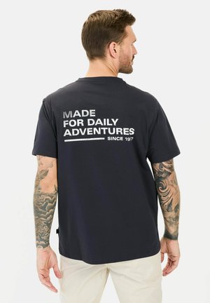 Navyblaue Baumwoll-T-Shirt mit kurzen Ärmeln; Text "FÜR TÄGLICHE ABENTEUER SEIT 1975" in Weiß auf dem Rücken. Sanfte Textur, lockere Passform.