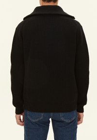 Svart stickad tröja med ribbat mönster, bred krage och långa ärmar. Kombinerad med mörkblå denimjeans i en avslappnad passform.