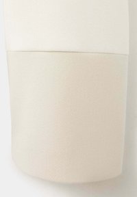 Détail du poignet d'une manche en tissu bicolore crème et blanc cassé avec une texture tissée subtile.