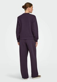 Lilla sweatshirt og matchende brede bukser lavet af blødt stof; har ribbede manchetter og kant samt et rundt halsdesign.