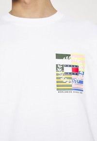 Witte t-shirt met korte mouwen, gekenmerkt door een kleurrijke grafische afbeelding op de borst met horizontale strepen, een kransontwerp en de tekst "TOMMY JEANS".