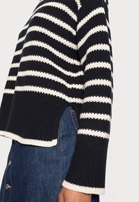 Marinblå och vit randig stickad tröja med långa ärmar, ribbade kanter och sidospalter. Tyget har ett texturerat, vävt utseende.