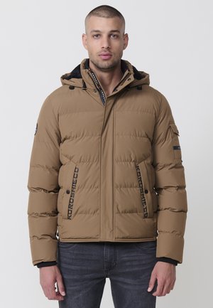 Veste matelassée marron avec capuche, accents noirs et détails en bandeau avec logo. Le matériau a une texture lisse avec un design ajusté.
