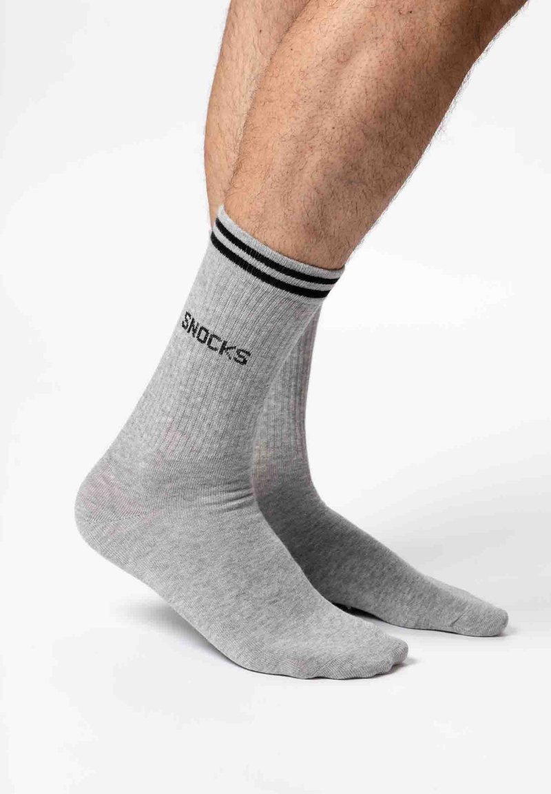 Graue, gerippte Socken mit schwarzen Streifen am Bund, auf der Seite steht das Wort "SNOCKS" in schwarzer Schrift.