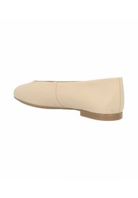 Zapato plano beige con punta redonda, parte superior de sintético suave, detalles de costuras mínimos y suela baja marrón. Diseñado para un uso fácil de poner y quitar.