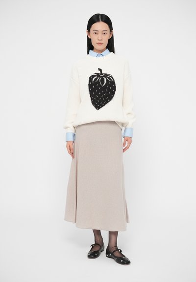 Camisola branca com um gráfico de morango preto, combinada com uma camisa azul clara e uma saia midi bege. Sapatos pretos com detalhes decorativos.