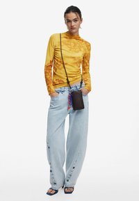 Maglietta gialla a maniche lunghe con motivo floreale, jeans a gamba larga blu chiaro con dettaglio dei bottoni e una piccola borsa a tracolla marrone con accenti vivaci.