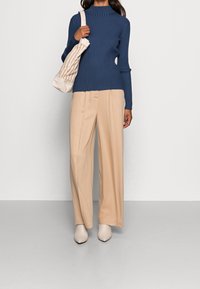 Námořnický žebrovaný rolák, béžové kalhoty s širokými nohavicemi a světlé lodičky s špičatou špičkou. Nese béžovou pruhovanou kabelku přes rameno.