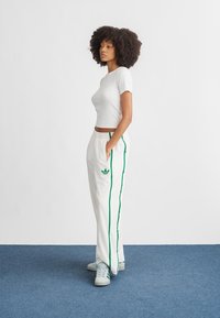 Valkoinen, lyhythihainen istuva paita, jotka yhdistyy valkoisiin joggereihin, joissa on vihreät sivuraidat ja adidas-logo. Tennarit ovat vaaleansiniset.