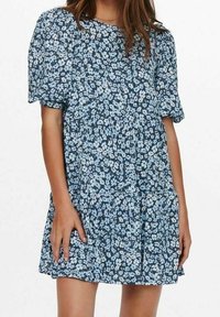 Květinové šaty v námořnické modři s krátkými vyp puff rukávy, představující jemný světle modrý květinový vzor a design sukně ve vrstvách. Měkká látka.