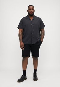 Korte mouwen zwarte knoopshirt, effen kleur, gecombineerd met zwarte shorts en zwarte schoenen, met omgeslagen manchetten en een ontspannen pasvorm.