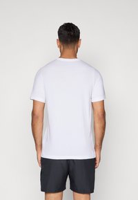 Balts kokvilnas T-krekls ar īsām piedurknēm, klasiskas apaļas kakla izgriezums un gluda faktūra, attēlots no aizmugures, valkāts kopā ar melniem šortiem.