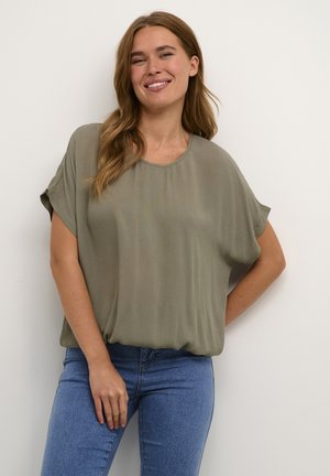 Top verde oliva a maniche corte con scollatura rotonda e vestibilità ampia, realizzato in un tessuto leggero e morbido; abbinato a jeans blu.