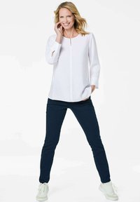 Top bianco a maniche lunghe con dettagli di bottoni frontali, abbinato a pantaloni aderenti blu scuro e sneakers bianche. Tessuto morbido e vestibilità comoda.