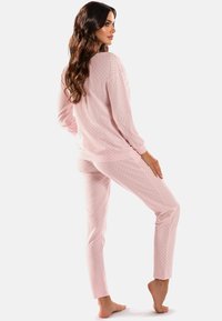 Rosafarbenes Pyjama-Set mit langen Ärmeln und Hosen, die kleine dunkle Polka-Dots aufweisen, aus weichem Stoff, mit lockerer Passform und rundem Ausschnitt.