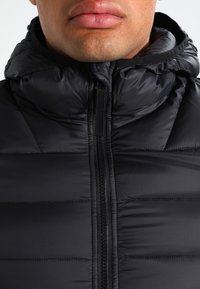 Schwarze Steppjacke mit hohem Kragen und Reißverschluss vorn. Verfügt über gesteppten Abschnitte, glatte Textur und ein leichtes, isoliertes Design.