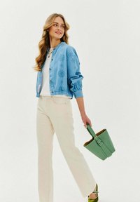 Světle modrá vyšívaná bomber bunda s kulatými knoflíky, bílý tričko, krémové kalhoty a zelená kabelka, doplněná zelenými podpatky.