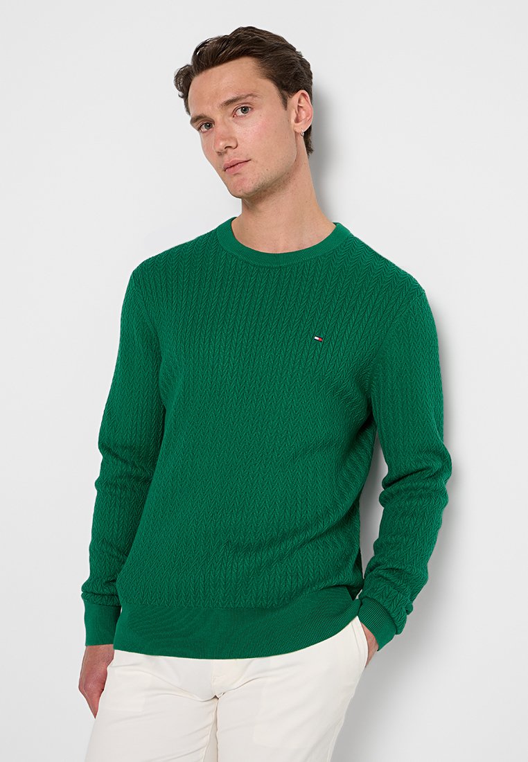 Groene gebreide trui met een gestructureerd diamantpatroon, ronde halslijn en een klein logoaccent op de borst. Lange mouwen en geribde manchetten.