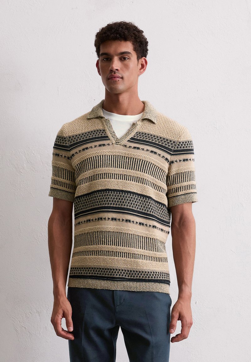 Koszulka polo z krótkim rękawem w jasnym beżu z czarnymi poziomymi paskami i wzorami. Posiada dekolt w serek i teksturowany materiał.