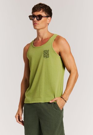 Grünes ärmelloses Tanktop mit feiner Struktur, rundem Ausschnitt und schwarzem Schriftzug auf der Brust. Kombiniert mit dunkelgrünen Shorts.