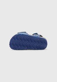 Blå sandaler med bølget gummisåle, med to justerbare stropper i en teksturert overdel. Mønsterdesign på stroppene gir detaljer.