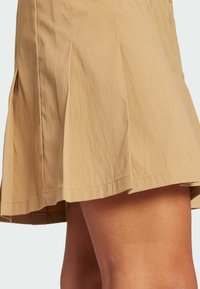 Tan pleated skirt made of lightweight fabric, featuring a textured surface and a hemline that falls above the knee.