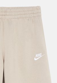 Beige Nike-Sweatpants mit elastischem Bund, ausgestattet mit einem weißen Logo auf dem linken Oberschenkel, gefertigt aus einem weichen Baumwollmischgewebe.