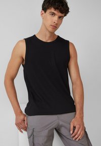 Schwarzes ärmelloses T-Shirt aus einer weichen Baumwollmischung, mit Rundhalsausschnitt und lässiger Passform, kombiniert mit hellgrauen Cargo-Hosen.