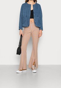 Jeansjacka med rundad halsringning och två framfickor, matchad med bruna och off-white rutiga utsvängda byxor med framknäppningar. Vita sneakers.