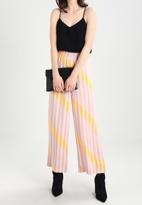 Černý top na tenkých ramínkách, široké kalhoty pruhované v růžové a žluté barvě, a černá kabelka. Modelka má na sobě černé boty na podpatku a kotníkové.