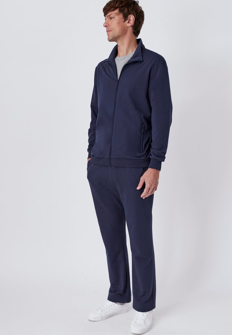 Survêtement bleu marine en tissu doux ; veste zippée avec col montant, manches longues et poches latérales ; pantalon assorti avec taille élastique.