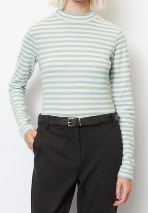 Osoba ubrana w jasnoniebieską koszulę w białe paski z długim rękawem, wpuszczoną do czarnych spodni z czarnym paskiem.