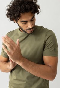 Olivgrünes T-Shirt mit kurzen Ärmeln aus weicher Baumwolle, mit Rundhalsausschnitt und einem kleinen Logoakzent auf dem linken Ärmel.