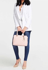 Vaaleanpunainen tikattu käsilaukku, jossa on kaksinkertaiset kahvat, kultaiset metalliosat ja metallinen logon koriste. Yhdistetty valkoiseen bleiseriin, sinisiin farkkuihin ja beigen värisiin korkoihin.