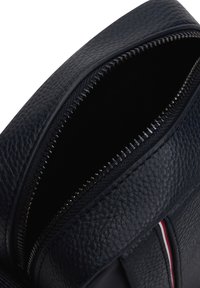 Laivastonsinisen nahkarepun vetoketju auki, esittelee teksturoidun materiaalin ja sisävuoren. Varustettu hopeansävyisellä vetoketjulla ja kontrastivärisellä raidalla.