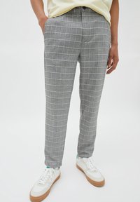 Pantaloni grigi a scacchi con motivo a griglia, realizzati in un materiale leggero, abbinati a sneakers bianche. Presentano una tasca frontale e una chiusura con bottone.