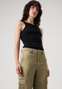 Zwarte geribbelde tanktop gecombineerd met kaki cargobroek met voorklepzakken en een gladde textuur. Gouden kettingaccent zichtbaar.