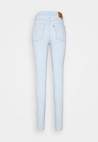 Jeans ajustados de color azul claro con una textura suave, que cuentan con un parche de cuero color bronce en la parte posterior, dos bolsillos traseros y sutilezas en el detalle de la costura.