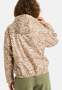 Gevoerde jas met patroon, voorzien van een beige achtergrond met witte bloem- en golflijnontwerpen. Elastische onderkant en manchetten, lichtgewicht materiaal.
