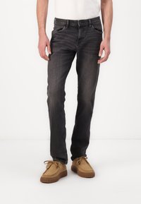 Jean en denim gris à coupe classique, avec un style cinq poches et un léger dégradé. Associé à des chaussures en suède beige.