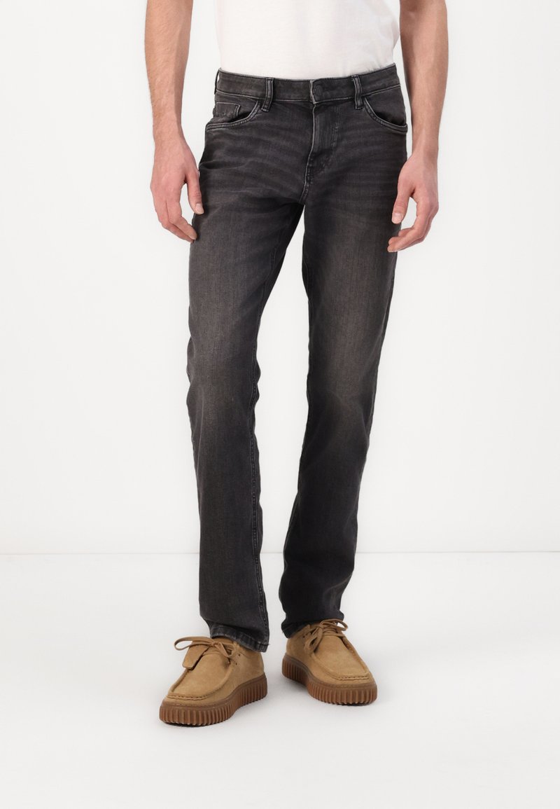 Jean en denim gris à coupe classique, avec un style cinq poches et un léger dégradé. Associé à des chaussures en suède beige.